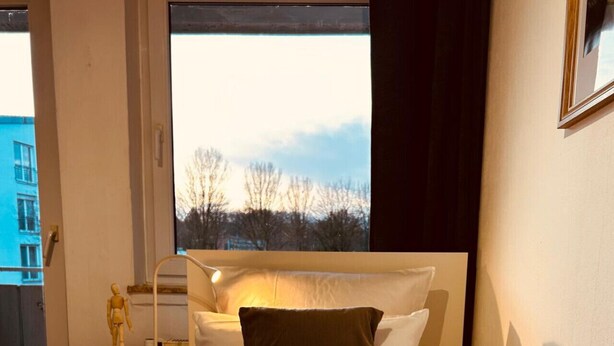 A neatly made bed with a rolled towel, a bedside lamp, and a nightstand with a small statue. - B23 Monteureiteamsi3zimmeritv (Ibbenbüren)