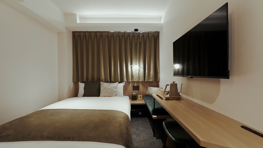 A hotel room with a bed, a desk, a television, and a window with curtains.