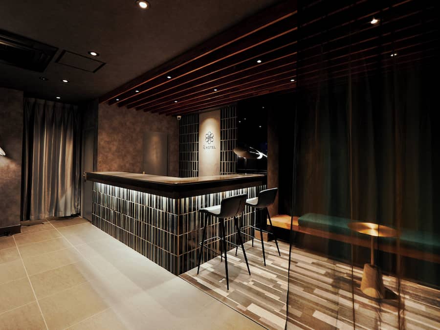 A modern hotel lobby with a reception desk, bar area, and seating.
