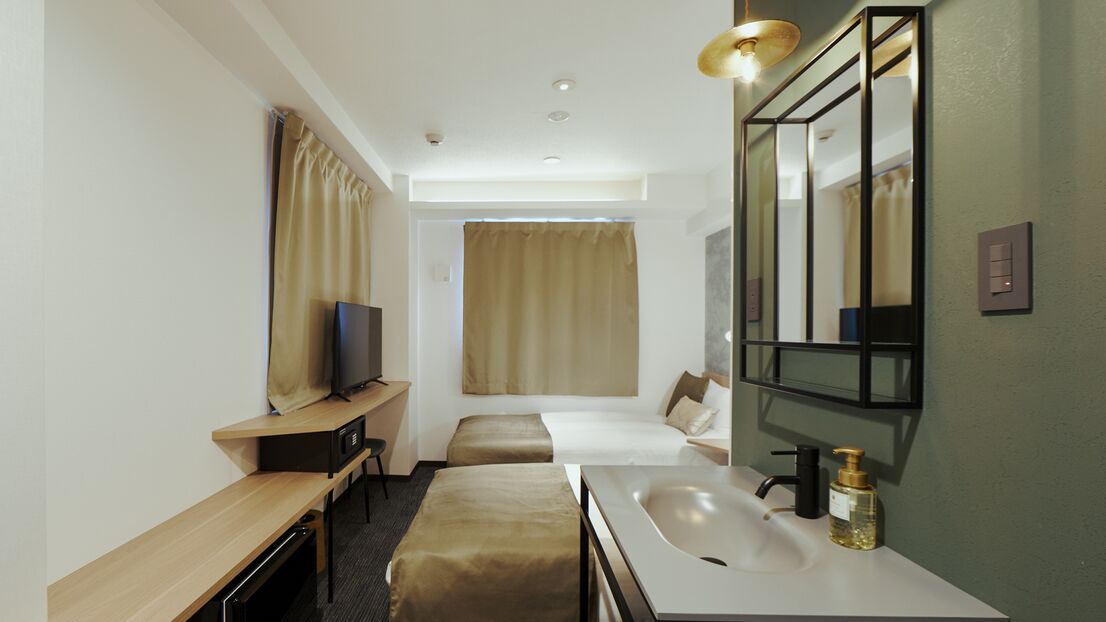 A hotel room with a bed, a desk with a chair, a television, a bathroom with a sink and mirror, and a window with curtains.