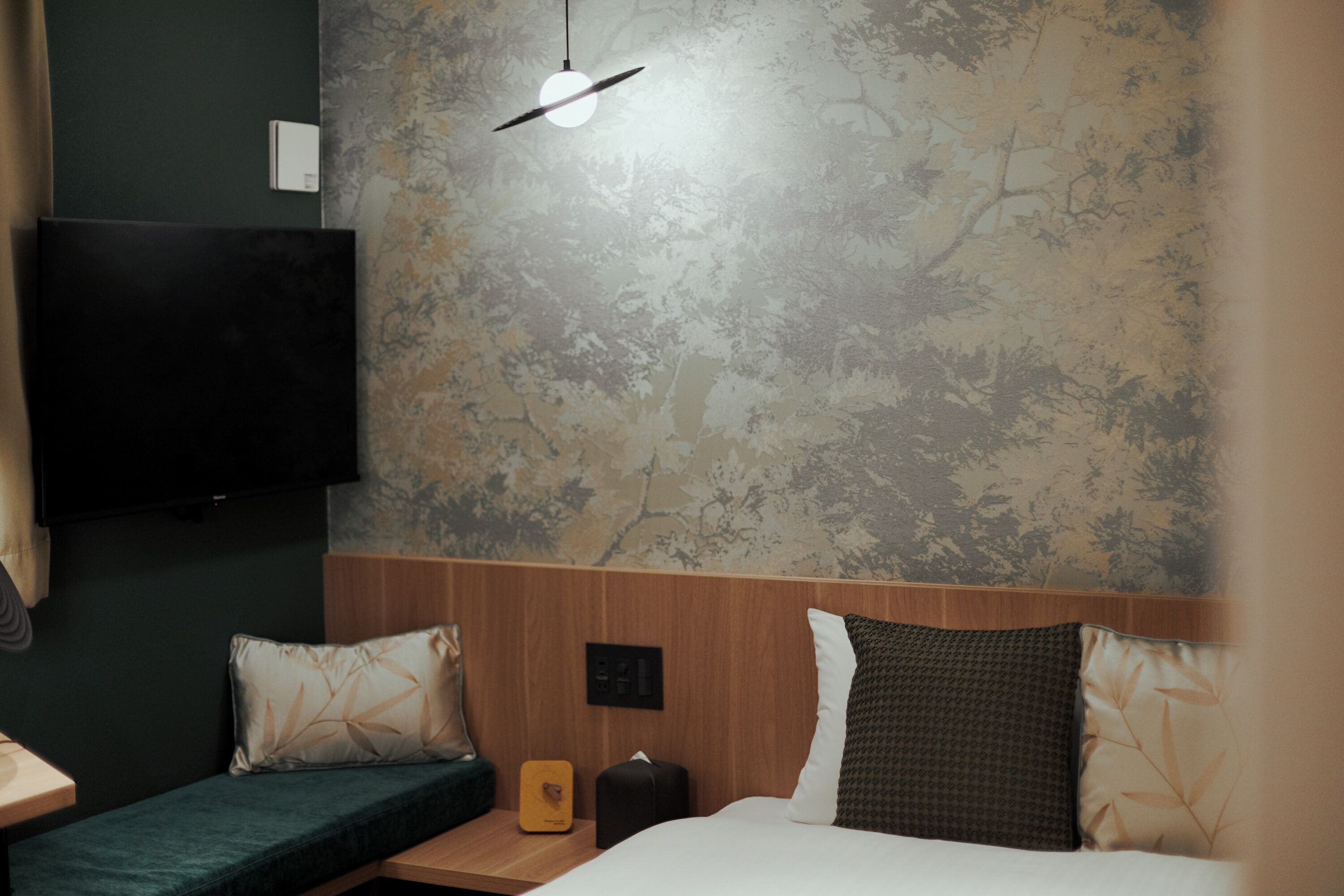 A hotel room with a bed, a bedside table, a lamp, and a wall-mounted TV.