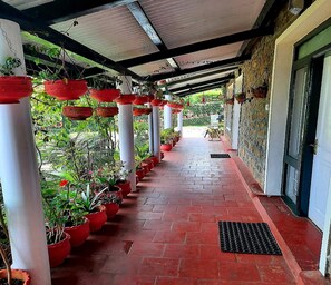 Un pasillo cubierto con plantas rojas en macetas y columnas blancas, que conduce a una puerta.