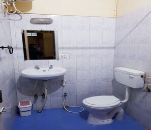 A small bathroom with a white sink, mirror, and toilet. There is a blue floor and a white trash bin. - Abu Residency (Kodaikanal)