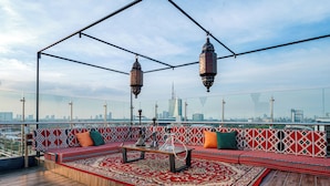A rooftop lounge with a patterned sofa, a coffee table, hanging lanterns, and a city view. - Excotel Design Hotel  (Surabaya)