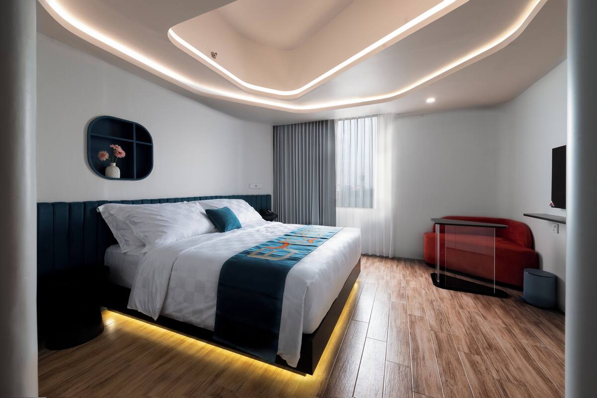 A modern hotel room with a bed, a red sofa, a TV, and a window with curtains.
