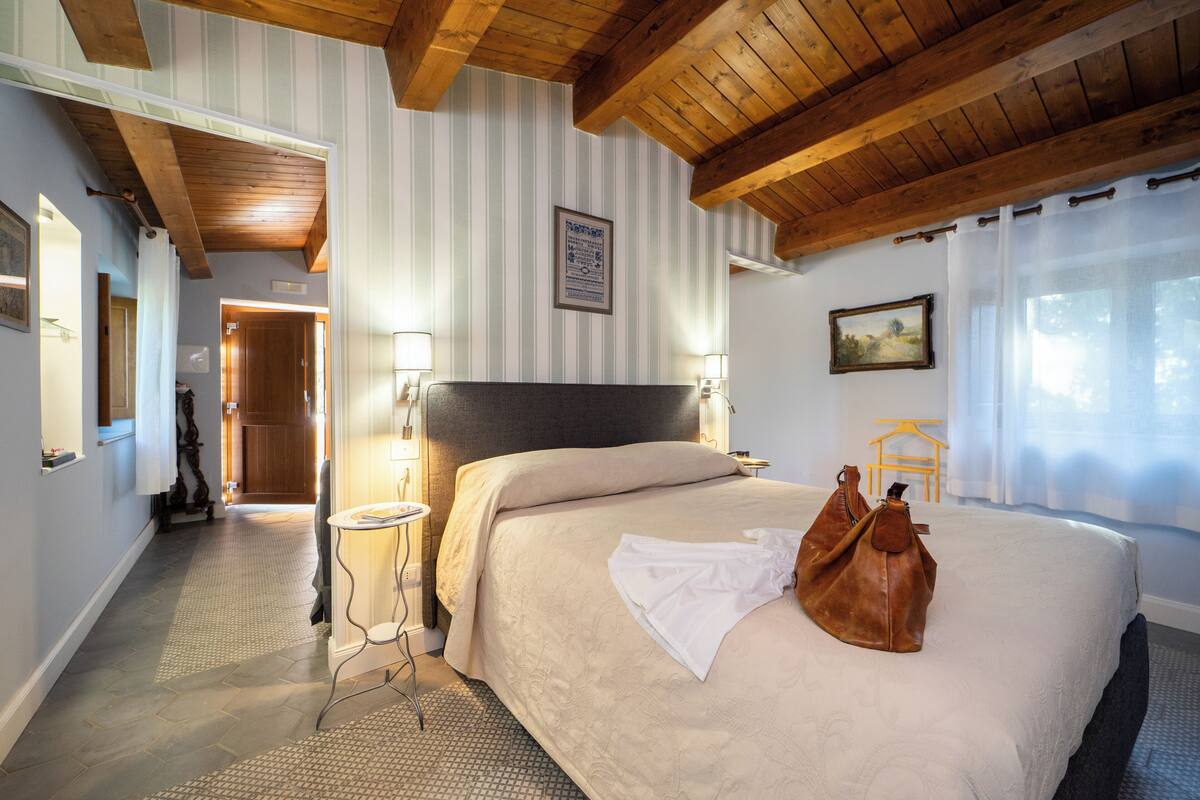 Ett hotellrum med en stor säng, synliga träbjälkar i taket, ett litet bord och ett sängbord med lampor.