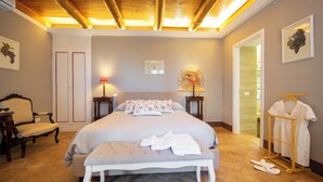 Un dormitorio con una cama grande, un banco, una silla, un armario y una percha para ropa.