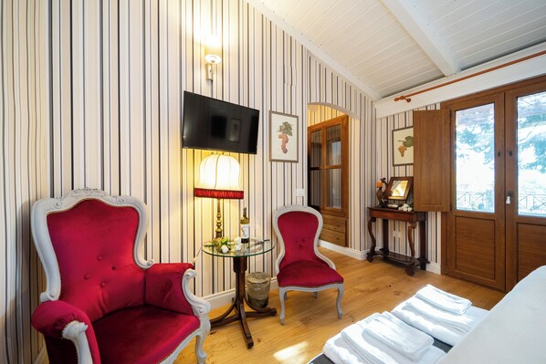 Une pièce avec un papier peint à rayures, un téléviseur, deux fauteuils rouges, une petite table avec une lampe et un lit avec des serviettes pliées.