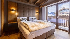 A bedroom with a large bed, wooden ceiling beams, a sliding glass door to a balcony, and two wall-mounted lights. - Chalet with 4 bedrooms (Ehrwald)