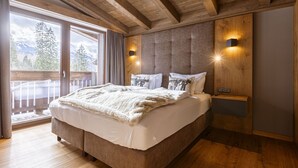 A bedroom with a large bed, wooden ceiling beams, a sliding glass door to a balcony, and two wall-mounted light fixtures. - Chalet with 3 bedrooms (Ehrwald)