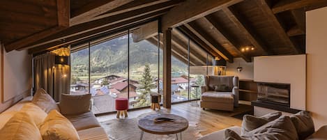 A spacious living room with a large window, wooden beams, a sofa, a coffee table, and a fireplace.