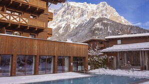 A wooden building with a pool in front, surrounded by snow-covered mountains.