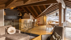 A spacious loft with a high ceiling, wooden beams, a kitchen area, and a dining space with a view of the outside.