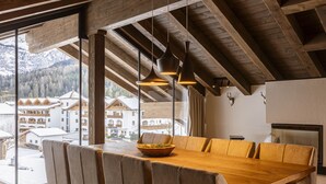 A dining area with a wooden table and chairs, large windows with a mountain view, and pendant lighting.