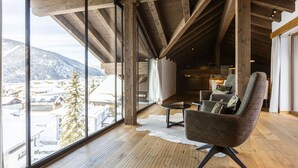 A spacious room with large windows, wooden beams, a cozy chair, and a small table. - Premium penthouse with 3 bedrooms (Ehrwald)