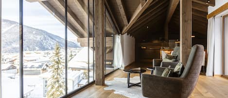 A spacious room with large windows, wooden beams, a cozy chair, and a small table.
