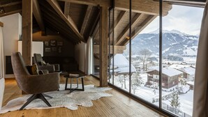 A spacious living room with a large window overlooking a snowy landscape, wooden beams on the ceiling, and a leather armchair. - Premium penthouse with 3 bedrooms (Ehrwald)