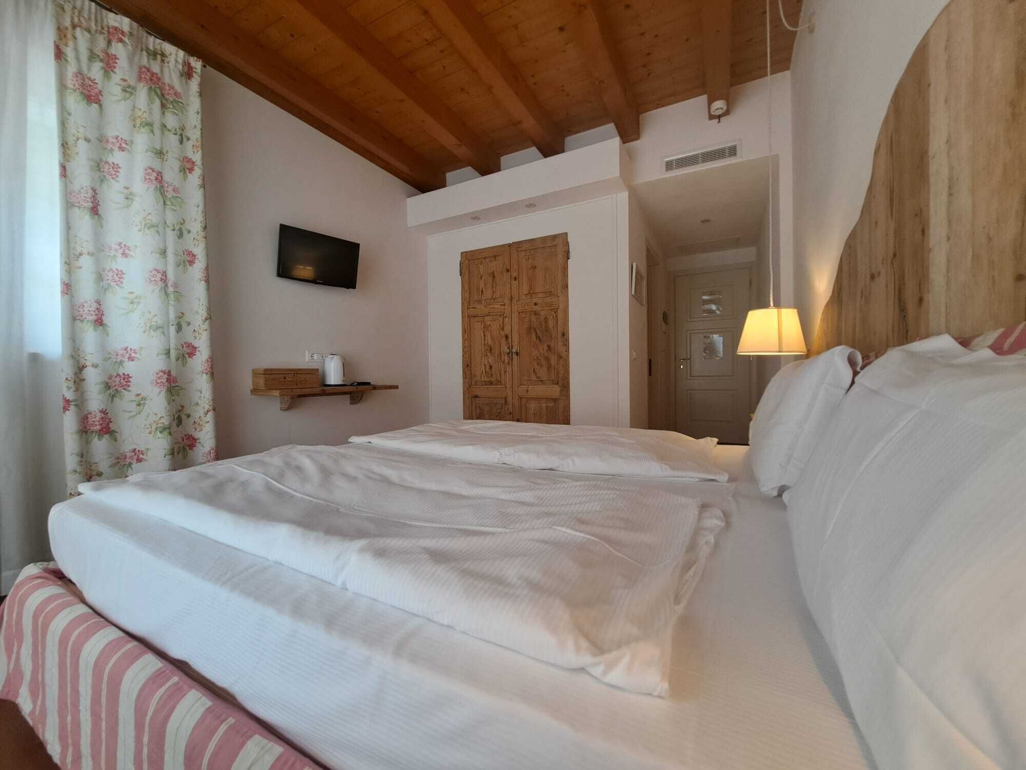 Un dormitorio con techo de madera, cama con ropa de cama blanca, armario de madera y televisor en la pared.