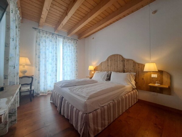 Een slaapkamer met een houten hoofdbord, twee bedlampen, een bed met een gestreept dekbedovertrek, een stoel en een bureau met een lamp.