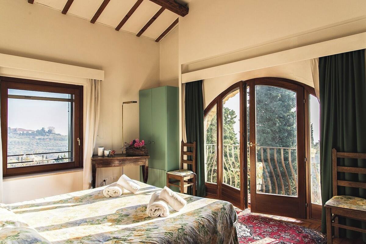 Ein Schlafzimmer mit Bett, Schreibtisch, Stuhl, Fenster und einem Balkon.