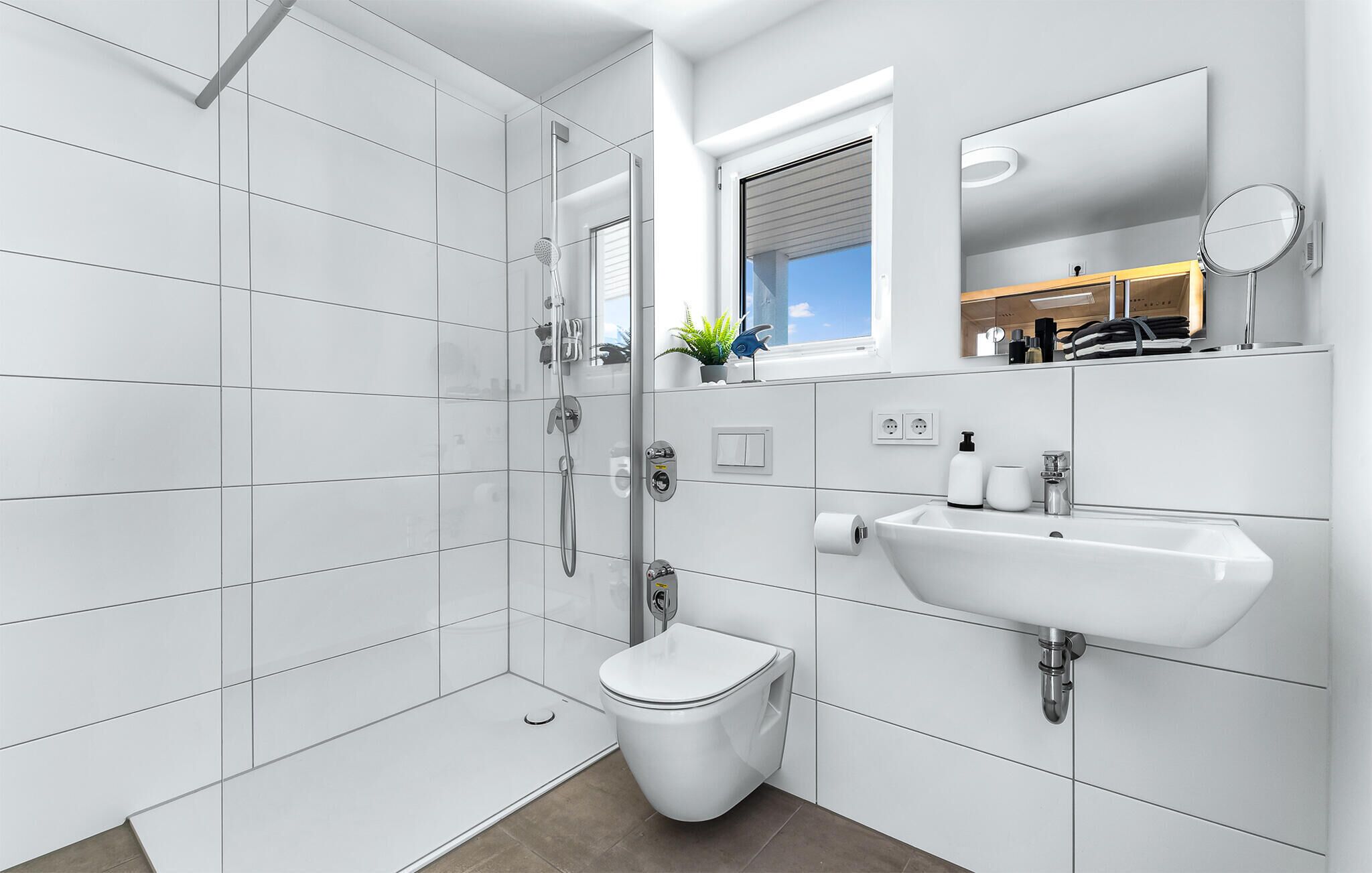 Un baño moderno con azulejos blancos, ducha, inodoro, lavabo y espejo.