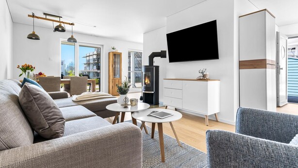 Ein modernes Wohnzimmer mit einer Couch, Sesseln, einem Fernseher, einem Kamin und einem Essbereich mit Tisch und Stühlen.