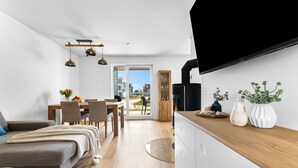 Ein moderner, kompakter Wohnraum mit Essbereich, einer Couch, einem an der Wand befestigten Fernseher und Blick durch die Tür.
