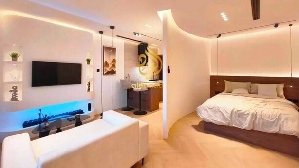 A modern hotel room with a flat-screen TV, a sofa, a bed, and a curved wall design.