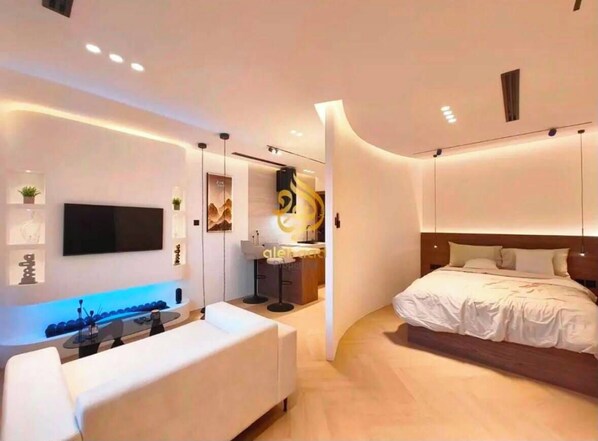 A modern hotel room with a flat-screen TV, a sofa, a bed, and a curved wall design.