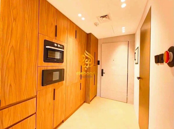 Un couloir avec des meubles de rangement en bois, un four encastré et une porte dotée d’une poignée.
