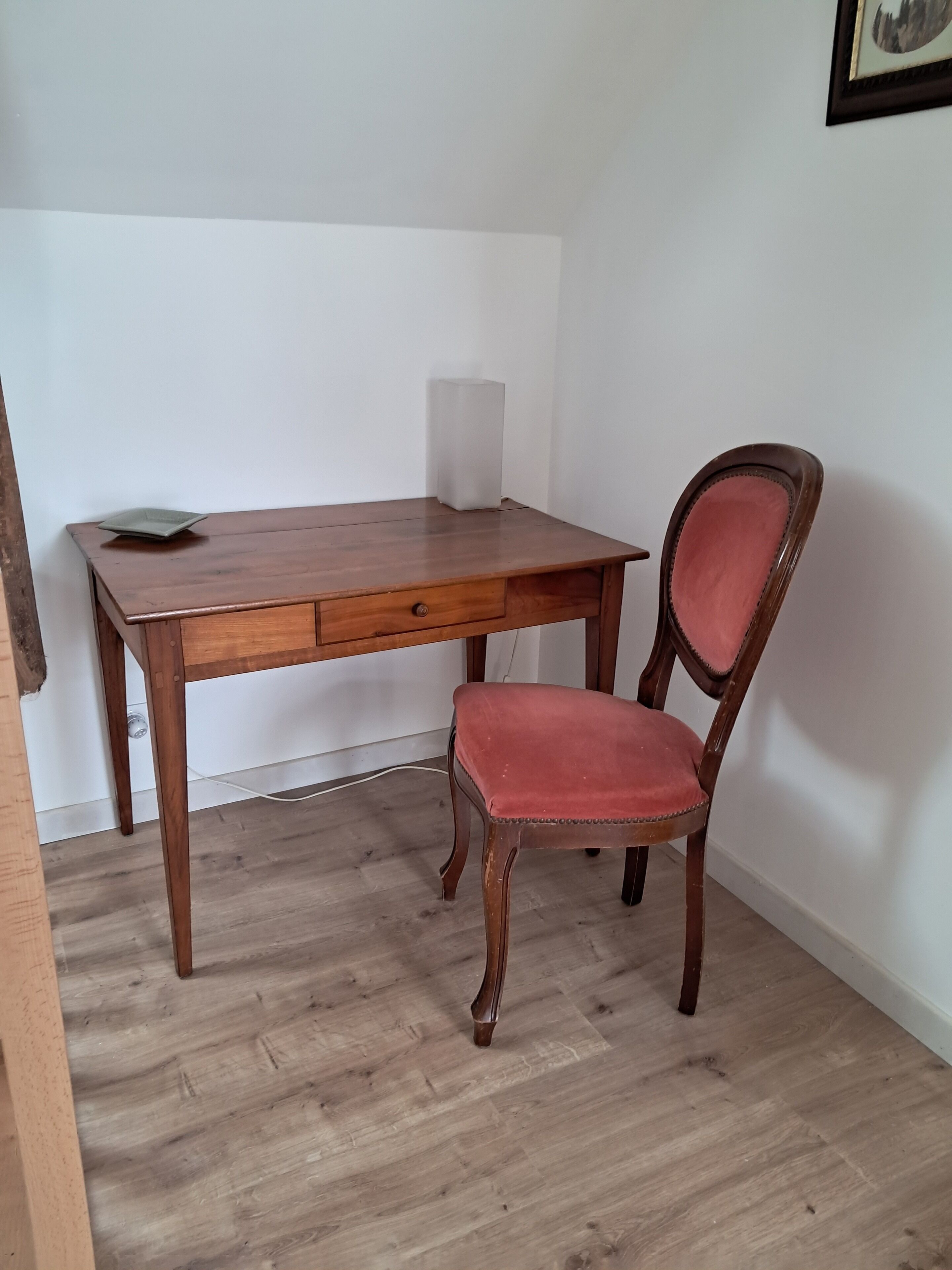 Een houten bureau met een lade en een stoel met een bekleed zitvlak.