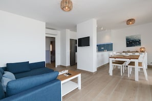 A modern living room with a blue sofa, a wooden coffee table, and a dining area with a white table and chairs.