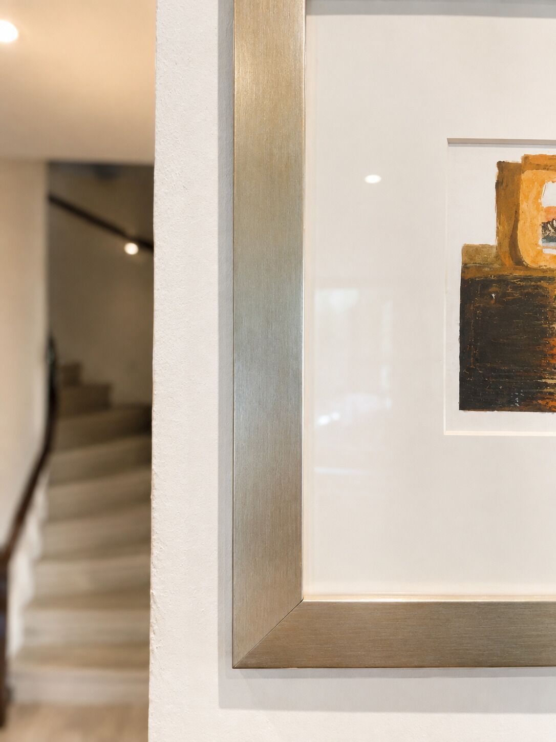A framed artwork on a wall with a staircase in the background.