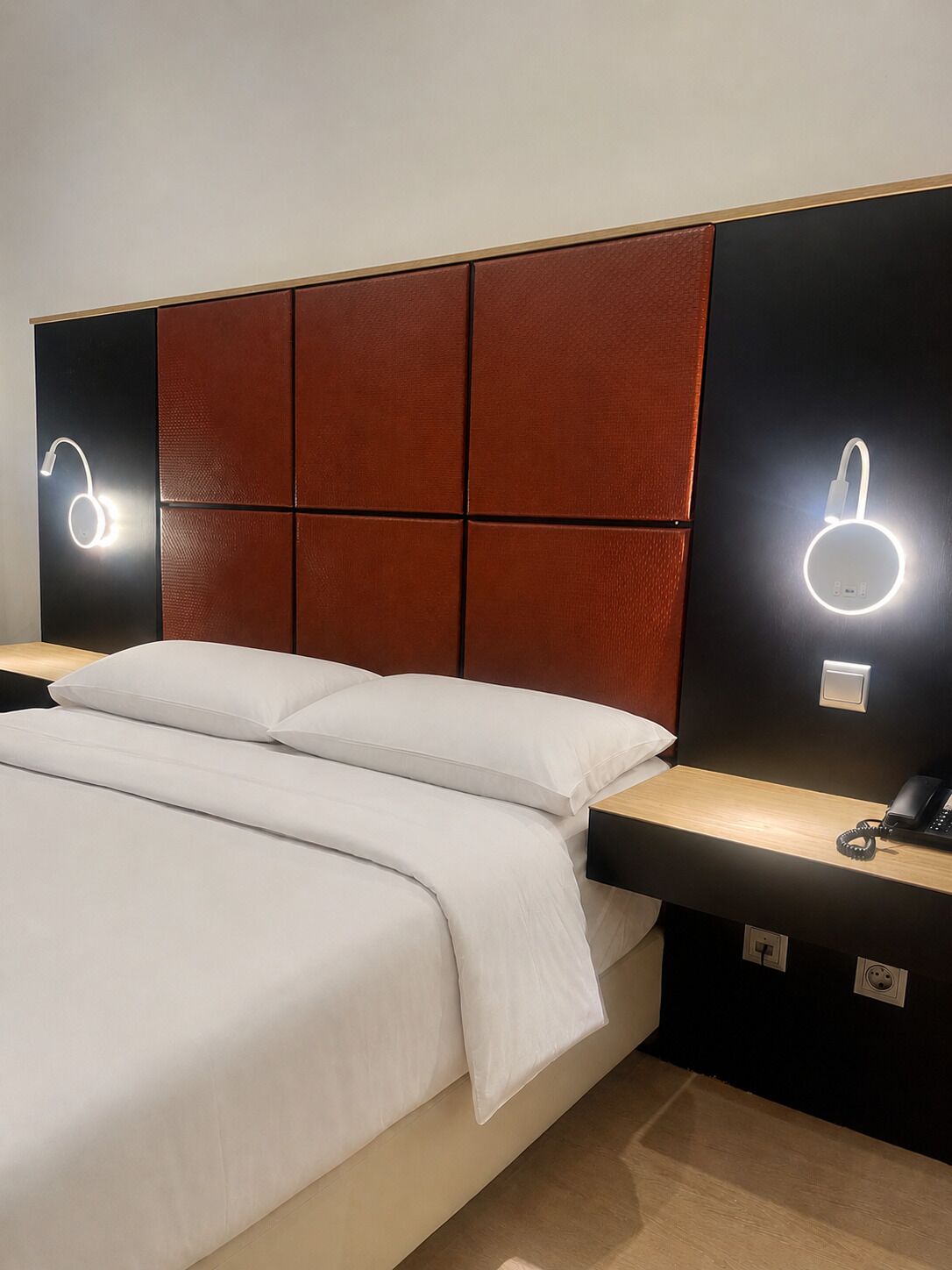 A modern hotel room with a bed, bedside tables, and illuminated wall sconces.