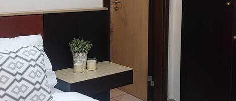 Una habitación de hotel ordenada con cama, mesita de noche y espejo.