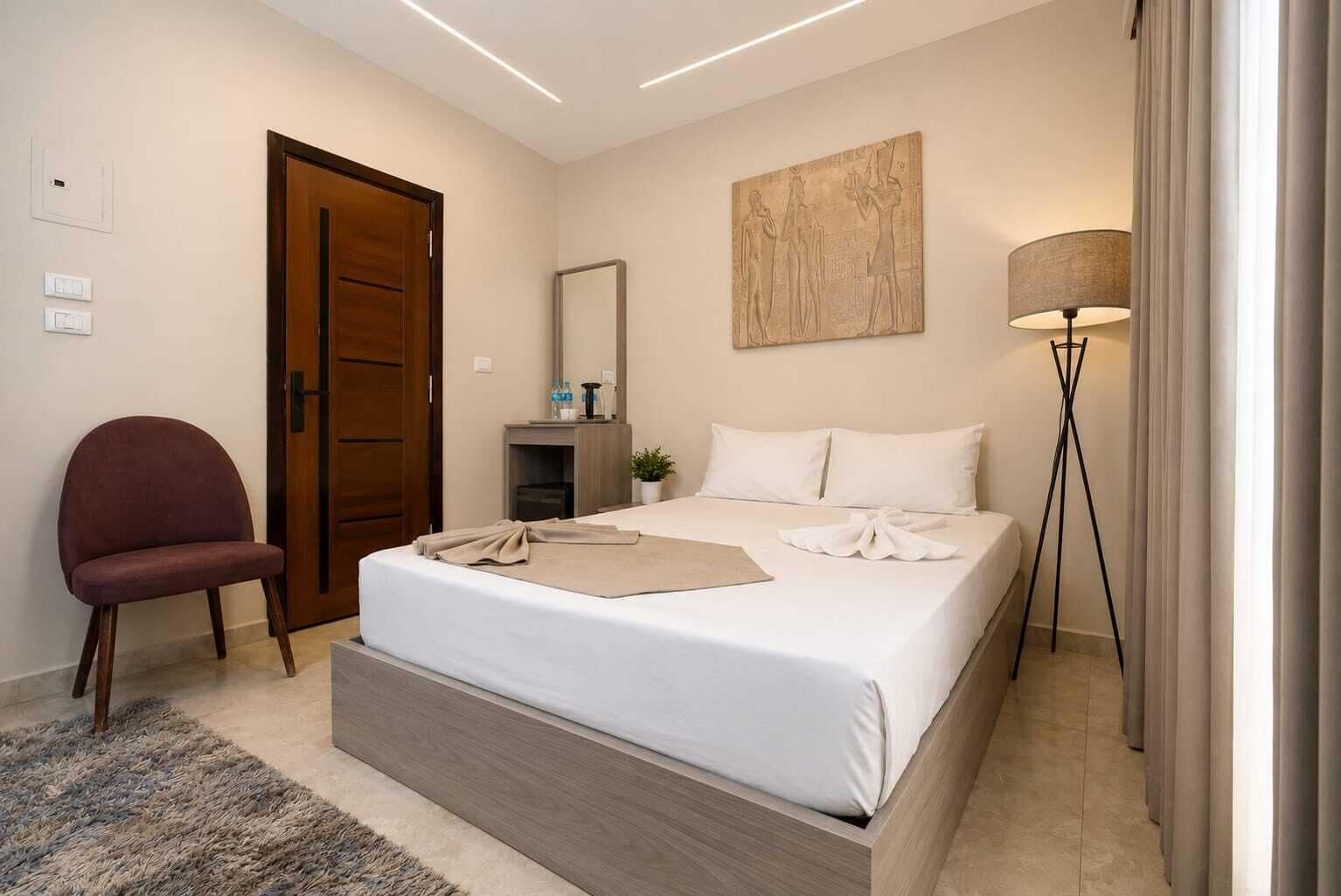 A hotel room with a bed, a chair, a desk, a lamp, and a door.