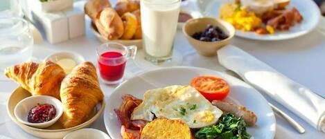 A breakfast table with croissants, eggs, bacon, toast, and a variety of spreads.