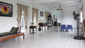 A spacious living room with patterned flooring, a wooden bench, a blue sofa, a standing fan, and a chandelier. - Moeimanee Resort (Mae Sot)