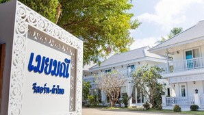 A sign with Thai text, a white building with balconies, and a tree in the background. - Moeimanee Resort (Mae Sot)