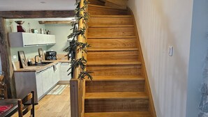 A wooden staircase with a rustic design, leading to a kitchen area with wooden cabinets and a dining table. - Restored barn in the heart of the Barousse valley (Ferrère)
