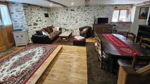 A cozy living room with a stone wall, a sofa, a coffee table, a dining table with chairs, and a television. - Restored barn in the heart of the Barousse valley (Ferrère)