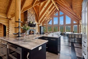 A log cabin interior with a stone fireplace, a large window, and a dining area.