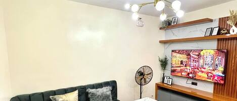 A modern living room with a sectional sofa, a dining table with chairs, a TV mounted on the wall, and a ceiling fan.