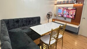 A modern living room with a sectional sofa, a dining table with chairs, a flat-screen TV mounted on a wooden cabinet, and a ceiling fan. - Seawind Condo 2 BR Free Wifi Near Samal (Davao)