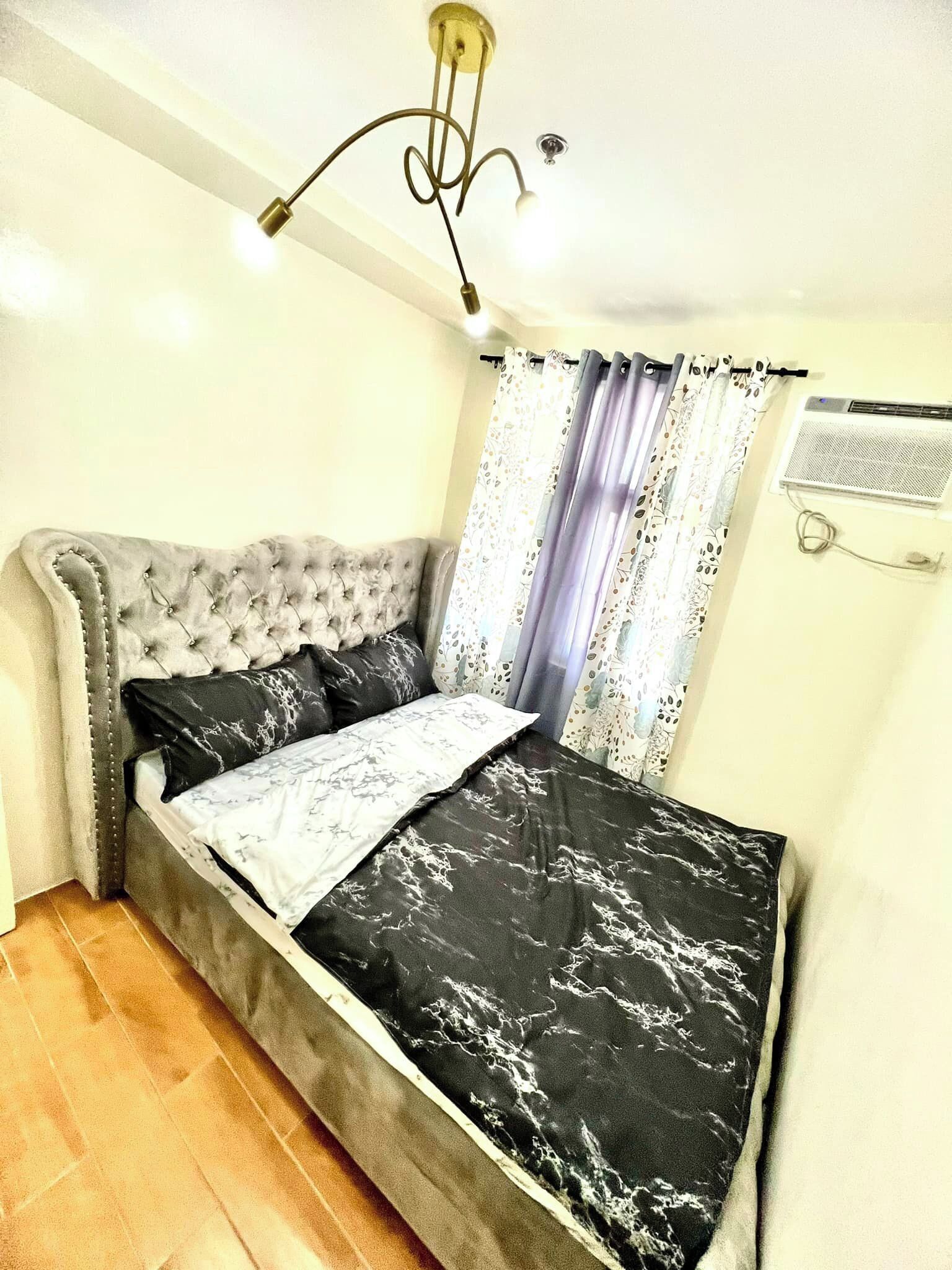 Une chambre à coucher avec une tête de lit capitonnée, un lit recouvert d’une couvre-lit en marbre noir et blanc, et un luminaire suspendu au plafond.
