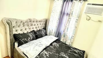 Une chambre à coucher avec une tête de lit capitonnée, un lit recouvert d’une couvre-lit en marbre noir et blanc, et un luminaire suspendu au plafond.