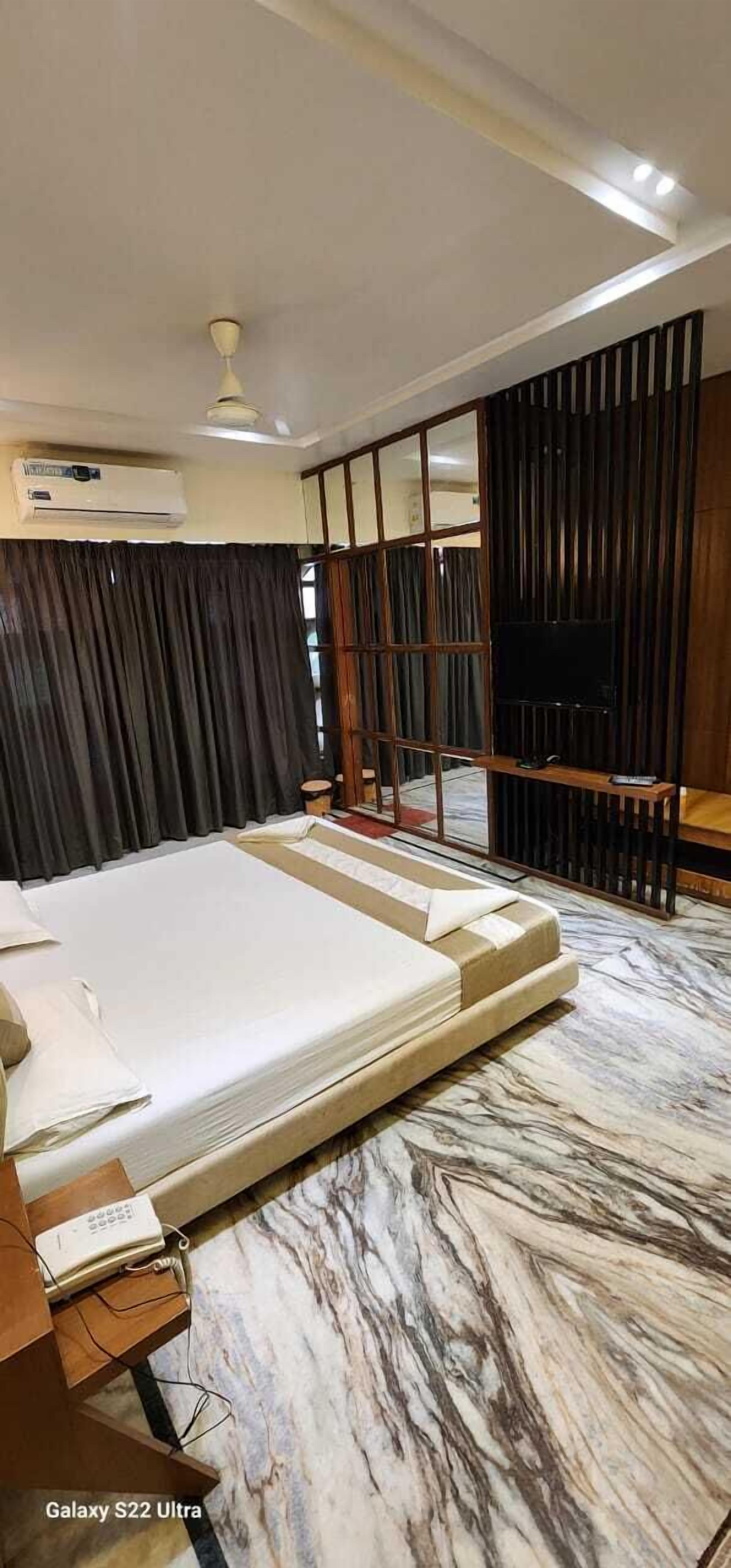 A hotel room with a large bed, a flat-screen TV, a ceiling fan, and an air conditioning unit.