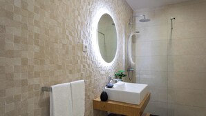 A modern bathroom with a large mirror, a freestanding shower, and a wooden vanity.