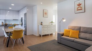 A modern living room with a grey sofa, yellow cushions, a dining table with chairs, a white cabinet, and a floor lamp.