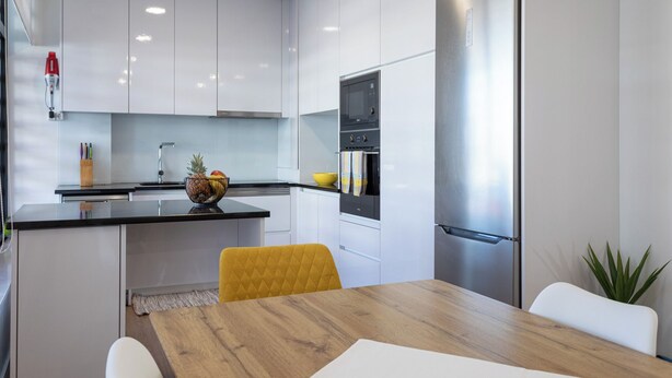 A modern kitchen with white cabinets, a stainless steel refrigerator, and a wooden dining table.